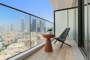 Ein Balkon mit Blick auf eine Stadtlandschaft, ein runder Tisch mit einer Pflanze und ein schwarzer Stuhl.