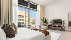 Ett modernt hotellrum med en stor säng, en TV och en balkong med utsikt över byggnaderna.