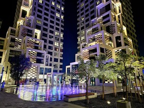 Un ensemble immobilier moderne, avec des fenêtres illuminées et une fontaine centrale.