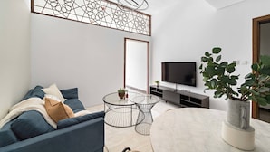 Un salon moderne avec un canapé, une table basse ronde, un téléviseur et un élément décoratif mural.