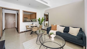Un salon moderne avec un canapé bleu foncé, une table basse en verre et un coin repas comprenant une table ronde et des chaises.
