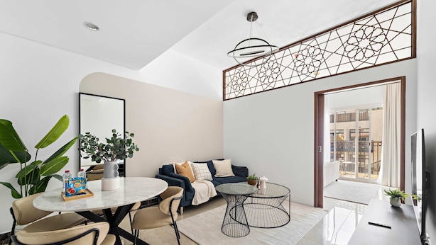 Un salon moderne comprenant un canapé, une table basse, une table à manger et des chaises. Une grande fenêtre offre une vue sur les bâtiments environnants.