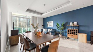 Een moderne eetruimte met een houten tafel en stoelen, een blauwe accentmuur en uitzicht op hoge gebouwen.