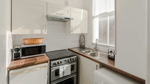 Eine kompakte Küche mit Mikrowelle, Herd und Spüle, ausgestattet mit weißen Schränken und einer Holz Arbeitsplatte.