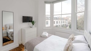 Ein Schlafzimmer mit einem Bett, einem großen Spiegel, einem Fernseher und einem Fenster mit Blick auf die Stadt.