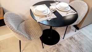 A dining table set with white plates, glasses, and cutlery, surrounded by two upholstered chairs. - Stayshort - Stunning Studio Unit in Business Bay That Sleeps 2 (Dubai)