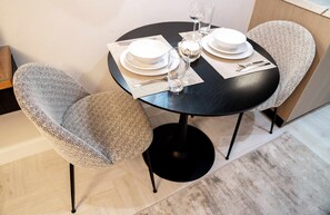 A dining table set with white plates, glasses, and cutlery, surrounded by two upholstered chairs. - Stayshort - Stunning Studio Unit in Business Bay That Sleeps 2 (Dubai)