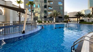 A swimming pool with a person in the water, surrounded by palm trees and modern buildings. - Stayshort - Stunning Studio Unit in Business Bay That Sleeps 2 (Dubai)