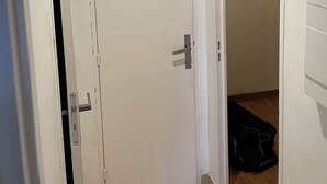 Ein Flur mit einer weißen, geschlossenen Tür, einer teilweise geöffneten Tür zu einem anderen Raum und einer schwarzen Tasche auf dem Boden.