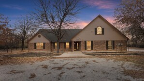 A two-story house with a brick facade, a large front porch, and a symmetrical window design. - Oakwood Oasis: 1.4 Acres Of Tranquility 6 Bedroom Home (Denton)
