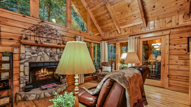 A cabin interior with a stone fireplace, leather sofa, and wooden walls. - Mountain Joy 1 Bedroom Cabin (Sevierville)