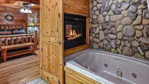 A log cabin interior with a stone wall, a fireplace, a wooden bench, and a hot tub. - Mountain Joy 1 Bedroom Cabin (Sevierville)