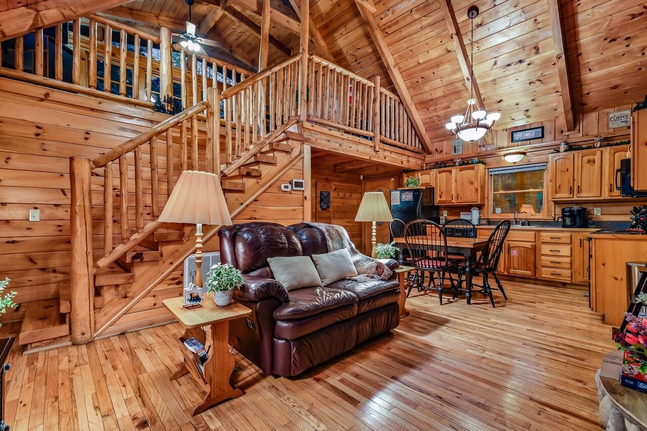 Ein Holzblockhaus-Interieur mit Ledersofa, Esstisch, Stühlen, Küchenzeile und einer Treppe.