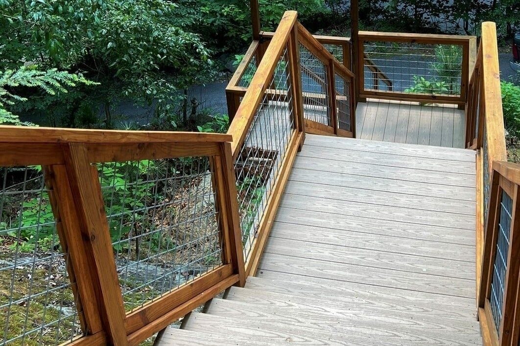 A wooden staircase leading to a deck surrounded by greenery.