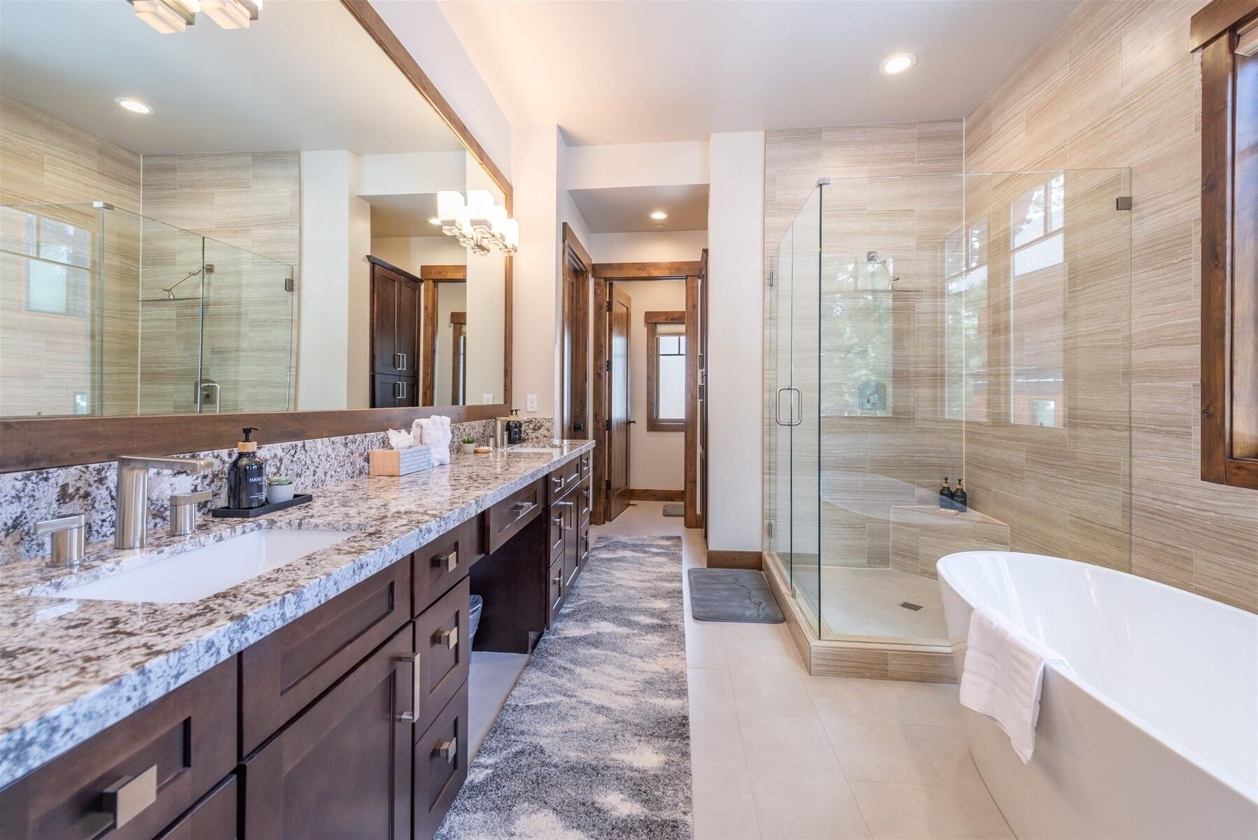 A modern bathroom with a large mirror, a walk-in shower, a bathtub, and a granite countertop.