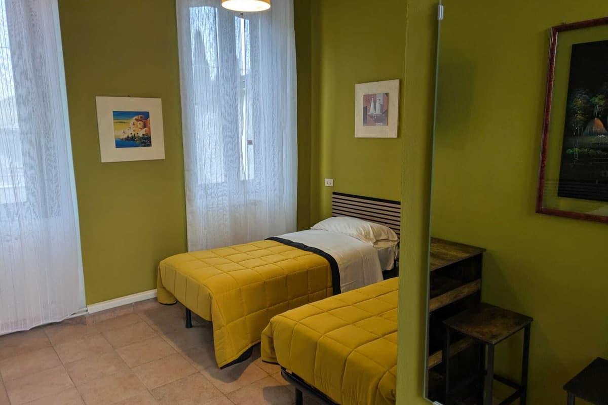 Une chambre avec deux lits, une fenêtre avec des rideaux légers, une table de chevet et un miroir.