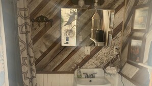Et badeværelse med træloft, hvid vask, spejl og toilet.