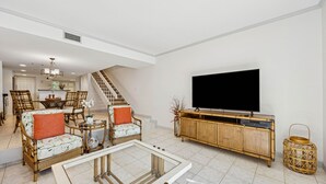 Een ruime woonkamer met een grote flatscreen-tv, rieten meubels en een trap naar een ander niveau.