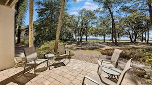 Een terras buiten met stoelen en tafels, omgeven door bomen en uitzicht op het water.