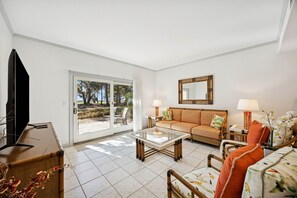 A living room with a sofa, coffee table, TV, and a sliding glass door leading to an outdoor area. - 3017 Club Villa Beautiful Golf Views (Fernandina Beach)