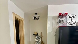 A hallway with a wooden door, a black refrigerator, and a patterned cloth hanging on a wooden rack.