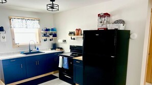 A modern kitchen with blue cabinets, a black refrigerator, and a window with a floral curtain.
