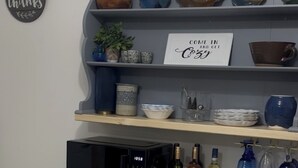A kitchen area with a microwave, wine bottles, and decorative bowls on shelves.