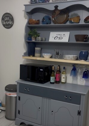 A kitchen area with a microwave, wine bottles, and decorative bowls on shelves.