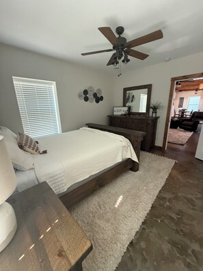 A bedroom with a bed, a dresser, a ceiling fan, and a window with blinds.