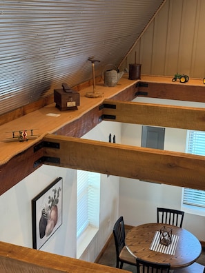 A loft-style room with wooden beams, a dining table with chairs, a small garden table, and a window with blinds.