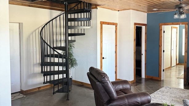 Amplia sala de estar con una escalera de madera, un sillón de cuero reclinable y una mesa de centro redonda.