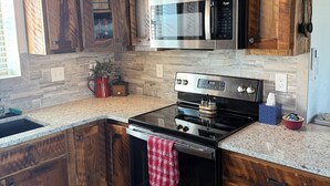 Una cocina con armarios de madera, un microondas de acero inoxidable, una estufa y encimeras de granito.