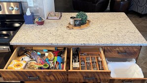 Una cocina con encimera de granito, cajones de madera y un cubo de basura empotrado.