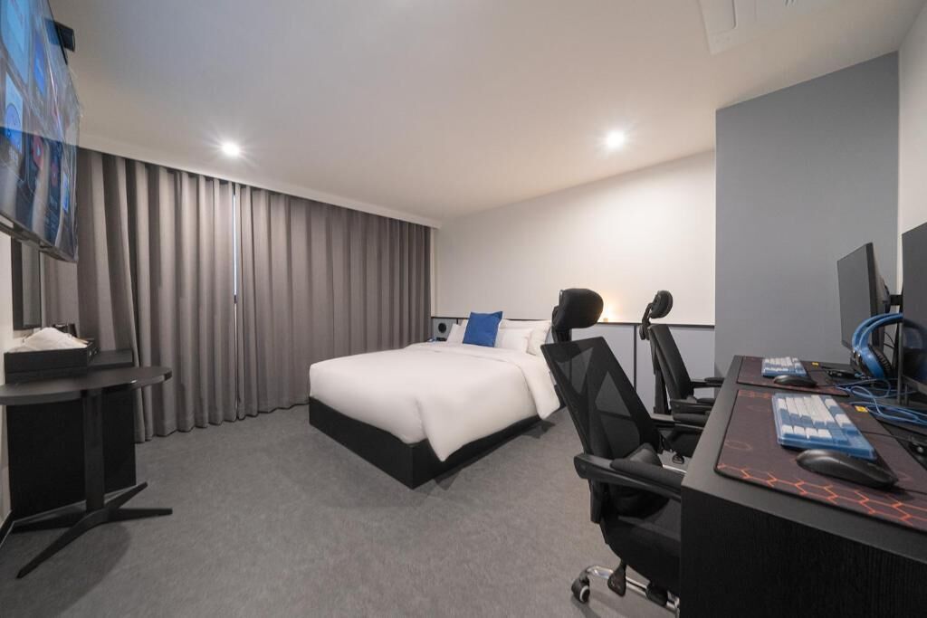 A hotel room with a bed, a desk with a computer, a chair, and a TV.