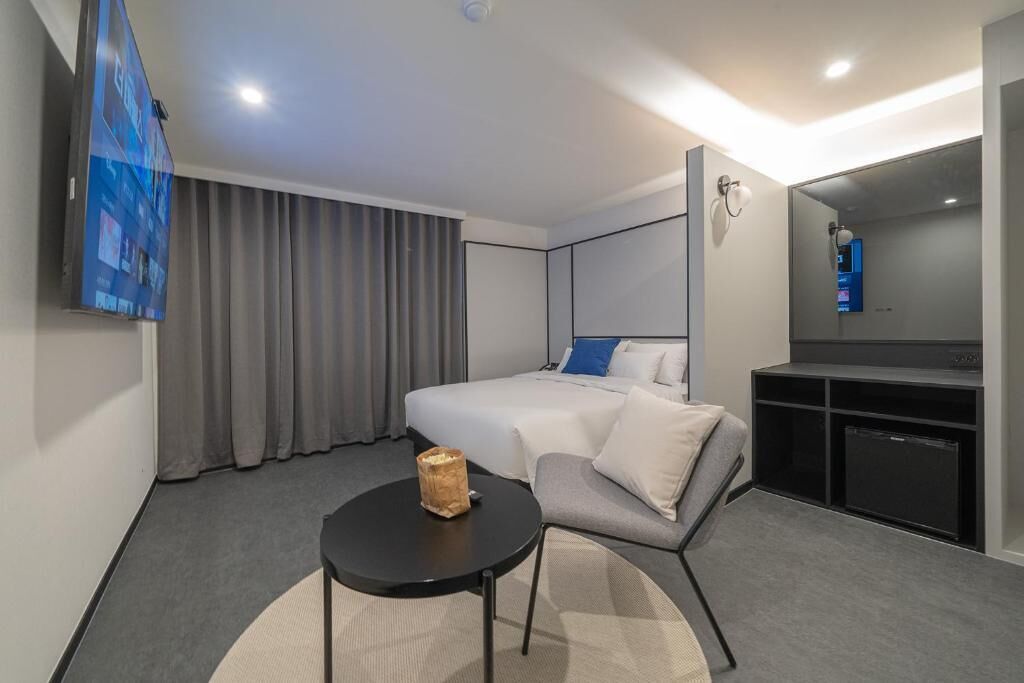 Ein modernes Hotelzimmer mit Bett, einem kleinen runden Tisch, einer Sitzecke, einem Fernseher und einem Spiegel.