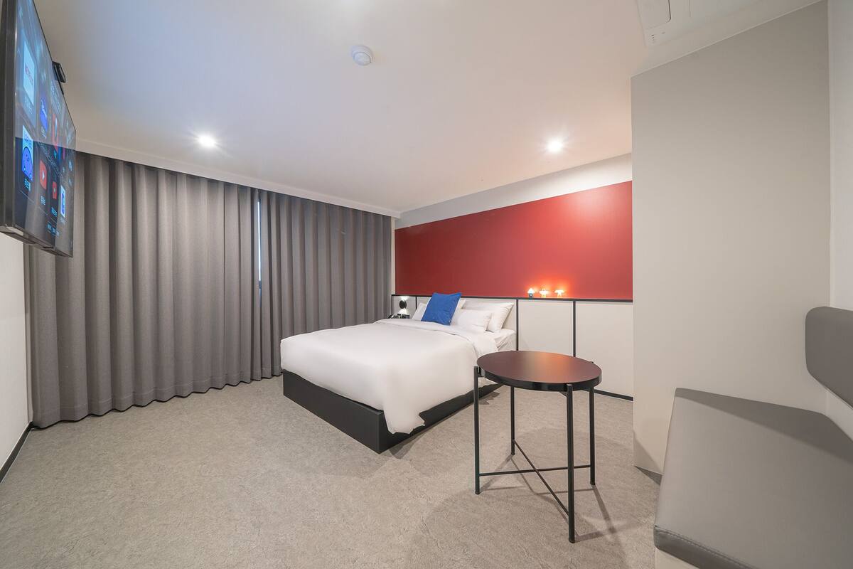 A modern hotel room with a large bed, a small round table, and a TV mounted on the wall.