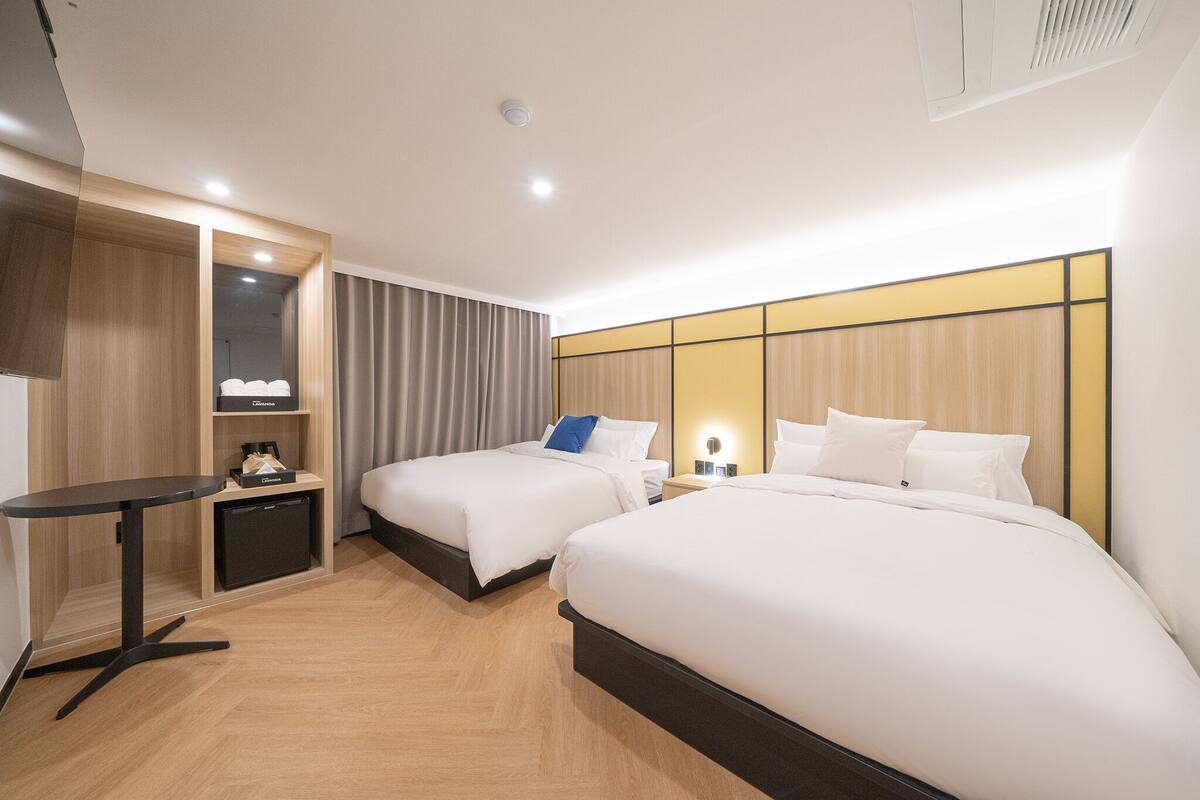 A hotel room with two beds, a small table, a desk, and a wardrobe.
