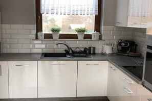 A modern kitchen with white cabinets, a built-in sink, and a window with blinds. - Holiday Home, Large Garden With Gazebo, Playground (Ustka)