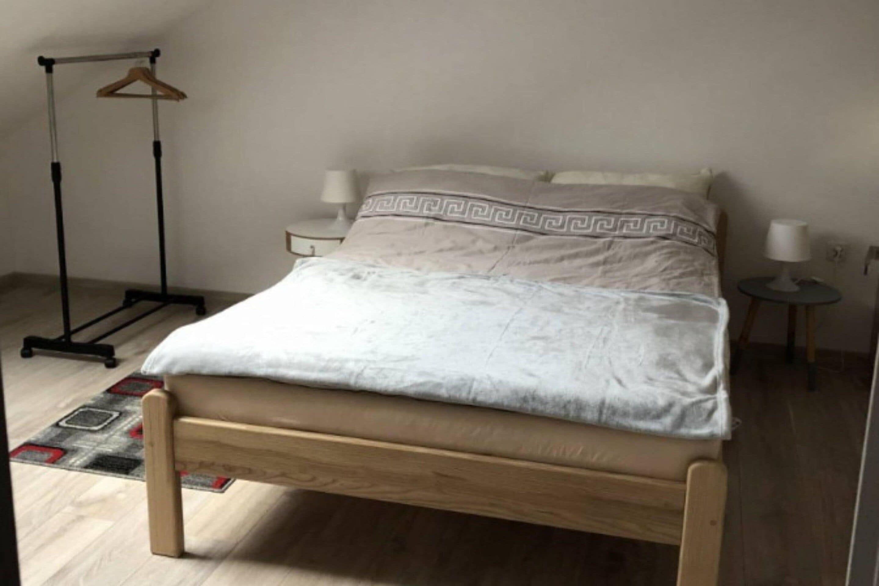 Une chambre à coucher comprenant un lit, une table de chevet, une lampe sur pied et un porte-vêtements suspendu.