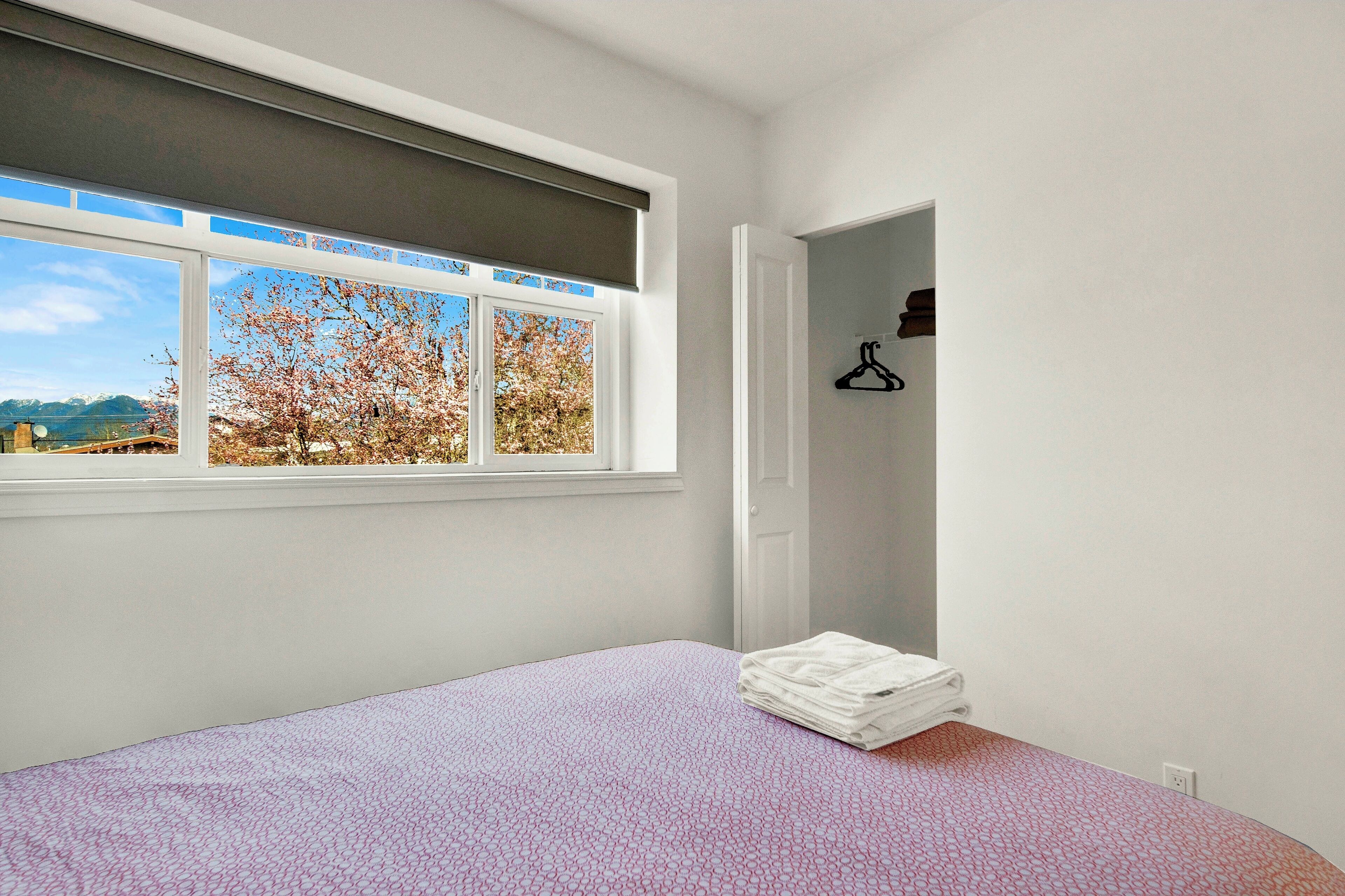 Ein Schlafzimmer mit einem Bett, einem Fenster mit Blick auf Bäume und einer Tür zu einem Kleiderschrank.