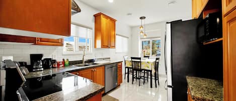 Una cocina con encimeras de granito, armarios de madera, un refrigerador de acero inoxidable y un comedor con mesa y sillas.