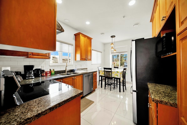 A kitchen with granite countertops, wooden cabinets, a stainless steel refrigerator, and a dining area with a table and chairs. - Three Bedroom Home Near YVR and Skytrain, Downtown Vancouver (Vancouver)