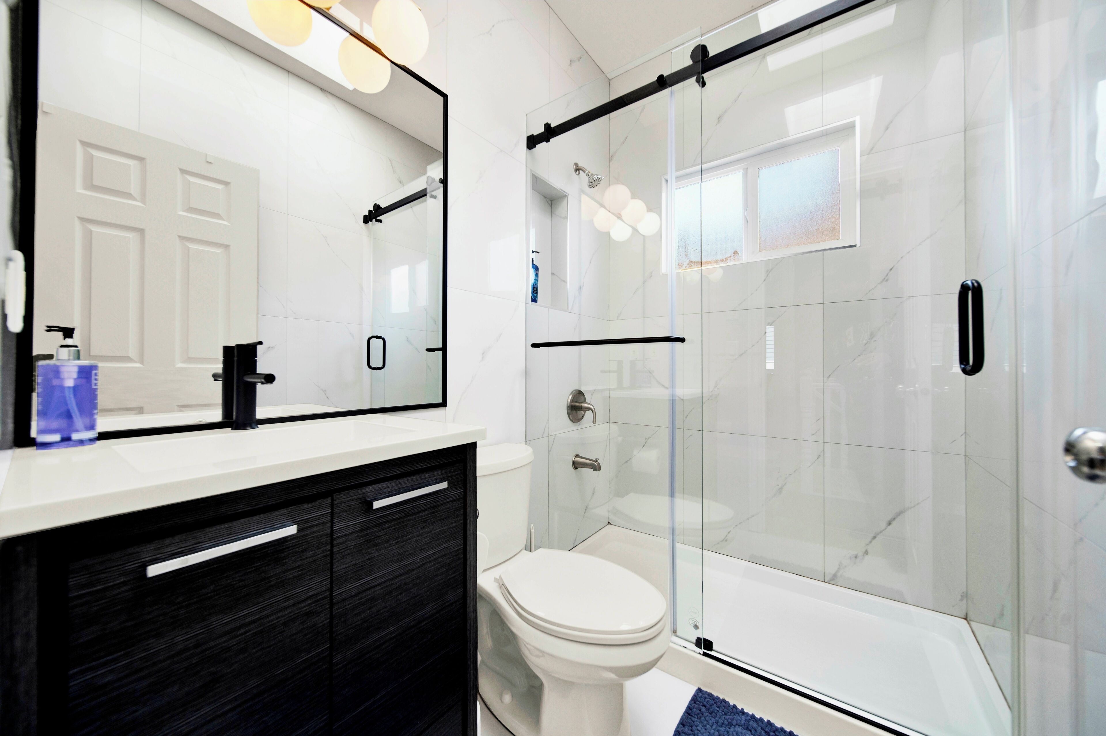 Un baño moderno con cabina de ducha de vidrio, inodoro blanco y un espejo grande con iluminación.