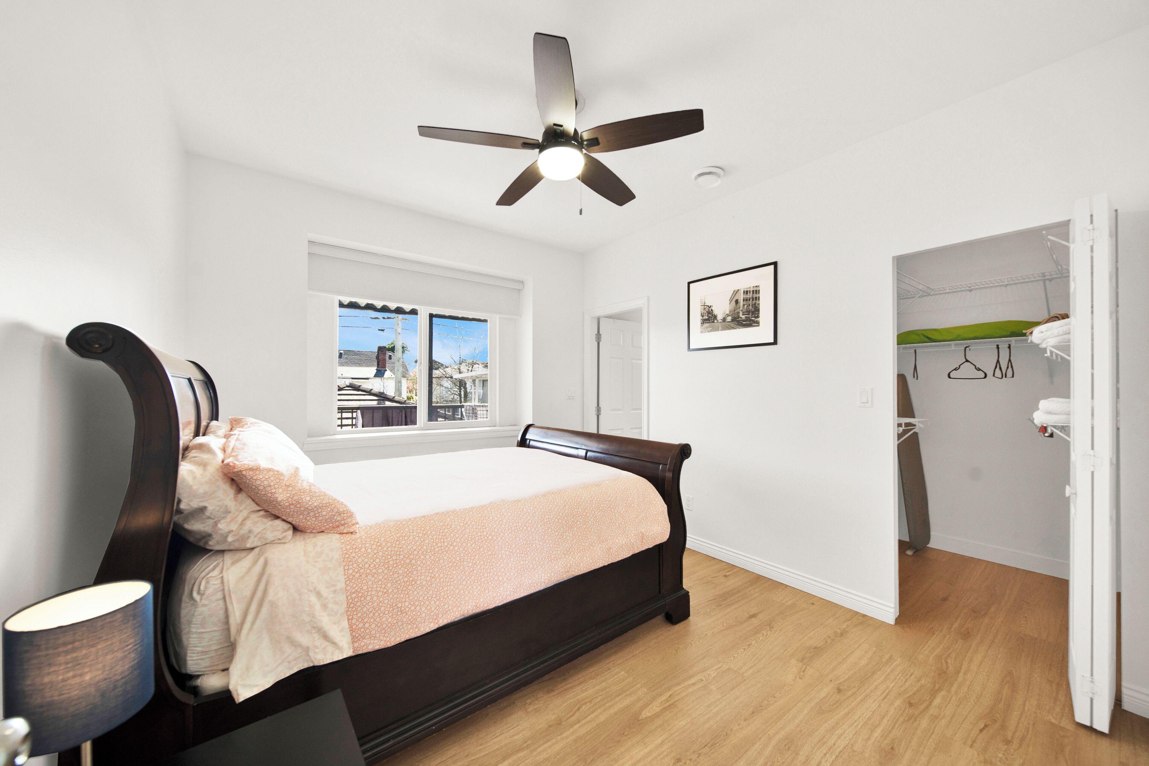 A bedroom with a bed, a ceiling fan, a window with a view, a door, and a closet.