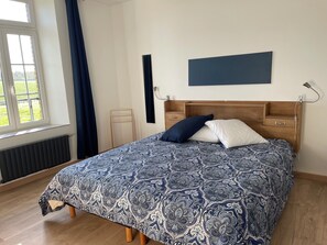 Un dormitorio con cama, mesita de noche, lámpara de pared y ventana con cortinas.
