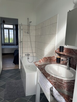 Un bany modern amb banyera, dutxa i un lavabo amb taulell de marbre.