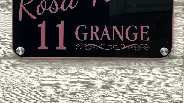 Un letrero negro con texto rosa y siluetas de mariposas, que dice "Rosa-Aurea 11 Grange".