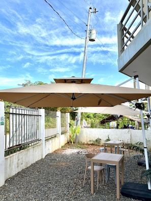 Un patio al aire libre con mesa y sillas, una zona de estar techada y una valla metálica.