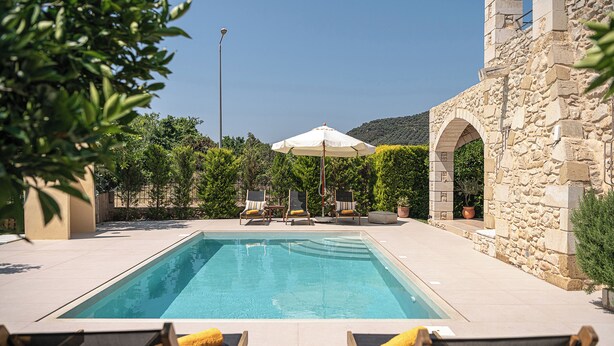 Une piscine avec des chaises longues et, en arrière-plan, un bâtiment en pierre.