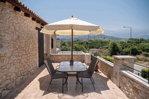 A stone building with a patio table and chairs, an umbrella, and a view of the countryside. - Elegant Countryside Retreat with Private Pool Near Chania (Kirtomados)